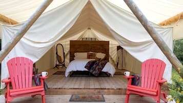 A tented accommodation with a bed, two red chairs, and a wooden floor.