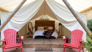 Eine Zelthütte mit einem Bett, zwei roten Stühlen und einem Holzboden.