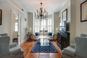 A living room with a sofa, two armchairs, a coffee table, a chandelier, and a fireplace. - Victorian Experience | Sleeps 6, Garden, 2‑Car Garage, Walk to Downtown (Savannah)