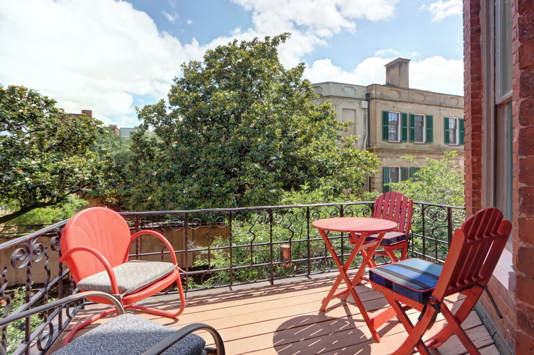 A balcony with outdoor furniture, a view of a river, and a building with green shutters.