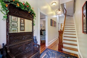 A staircase with wooden steps and a handrail, a mirror with framed pictures, and a chandelier. - Victorian Experience | Sleeps 6, Garden, 2‑Car Garage, Walk to Downtown (Savannah)