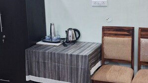 Une petite pièce avec une table, deux chaises, une armoire noire et un tableau accroché au mur.