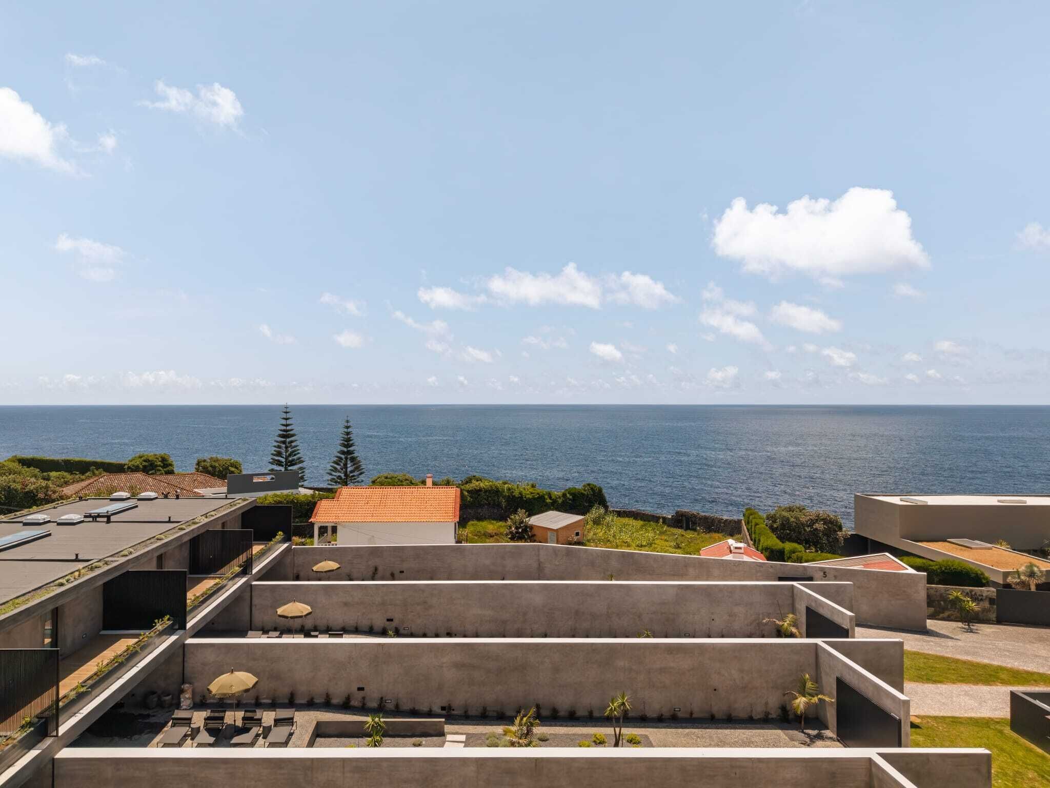 Una terraza en la azotea con vistas al mar, que presenta un diseño arquitectónico moderno con estructuras de concreto y vegetación.