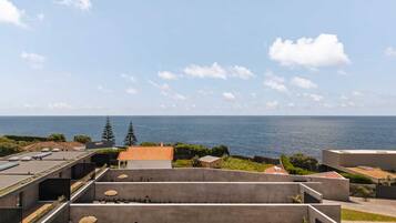Una terraza en la azotea con vistas al mar, que presenta un diseño arquitectónico moderno con estructuras de concreto y vegetación.