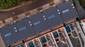 Eine Vogelperspektive zeigt ein Hotel mit mehreren Schwimmbecken, Sitzgelegenheiten im Freien und einem Parkplatz.