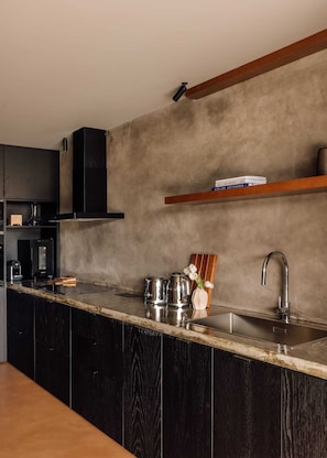 A modern kitchen with a dark wood cabinet, a stainless steel sink, and a wooden shelf above the countertop.