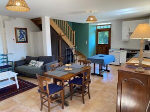 A cozy living room with a sofa, a dining table with chairs, a staircase, and a kitchen area. - Comfortable and quiet house, 2 bedrooms (Saint-Marcel-Bel-Accueil)
