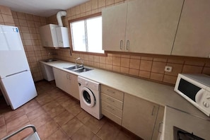 A compact kitchen with a washing machine, a microwave, and a refrigerator. - Spacious 3-room apartment right on the beach. Rodes-71 (Calafell)