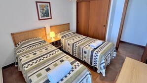 A room with two beds, a wooden wardrobe, a hanging lamp, and a framed picture on the wall. - Spacious 3-room apartment right on the beach. Rodes-71 (Calafell)