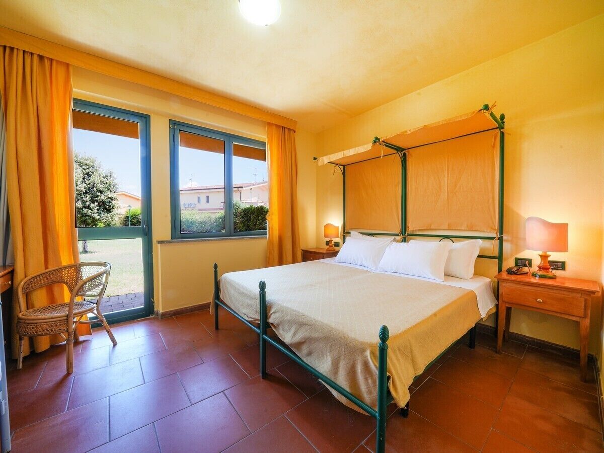 Une chambre à coucher comprenant un lit, une chaise, une table de chevet et une fenêtre avec des rideaux.