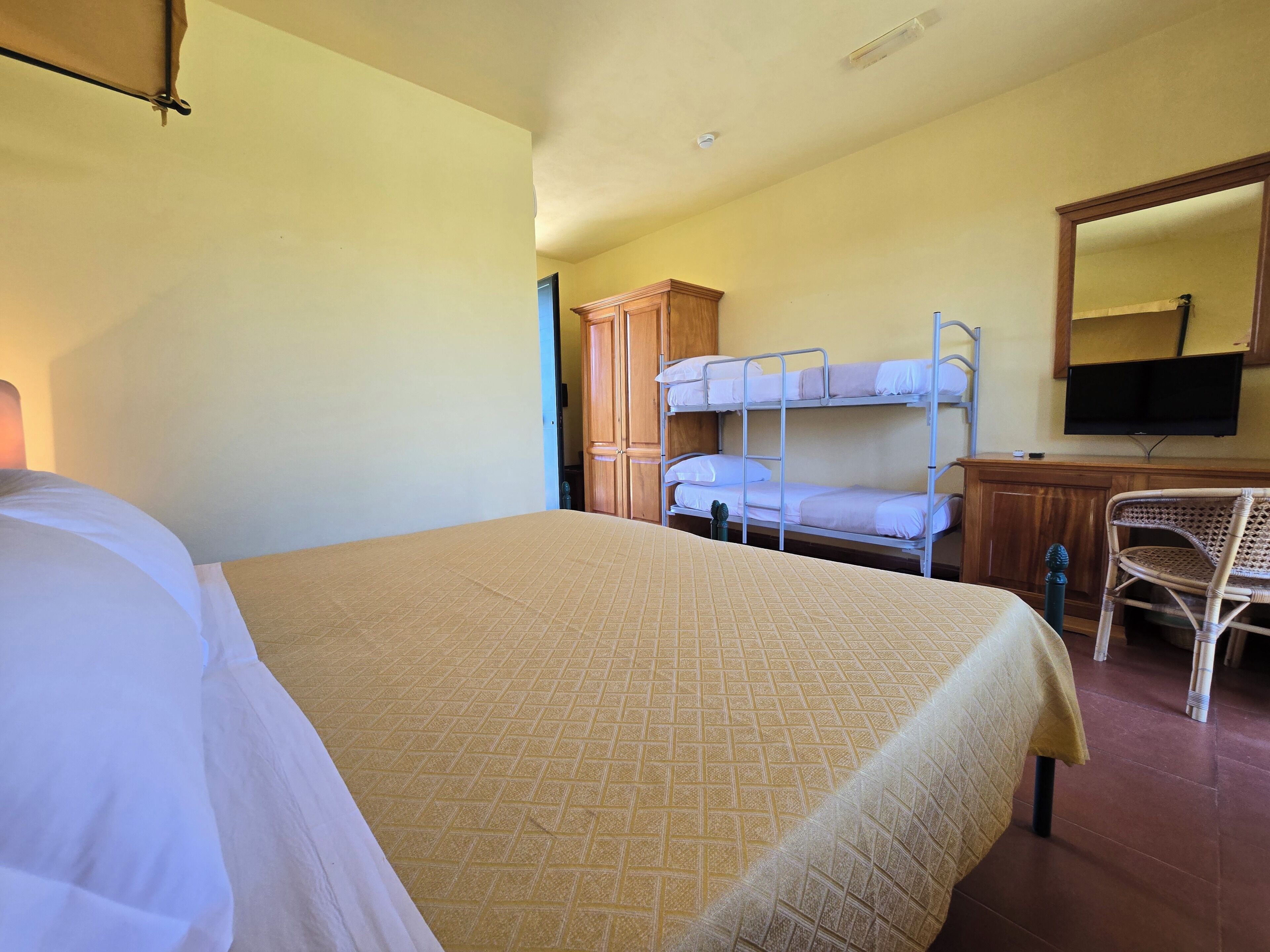 Una habitación de hotel con una litera, un escritorio con silla, un televisor y un armario.