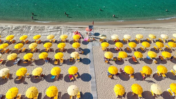 An aerial view of a beach with numerous yellow umbrellas and beach chairs arranged in rows. - Marina del Marchese Resort (Botricello)