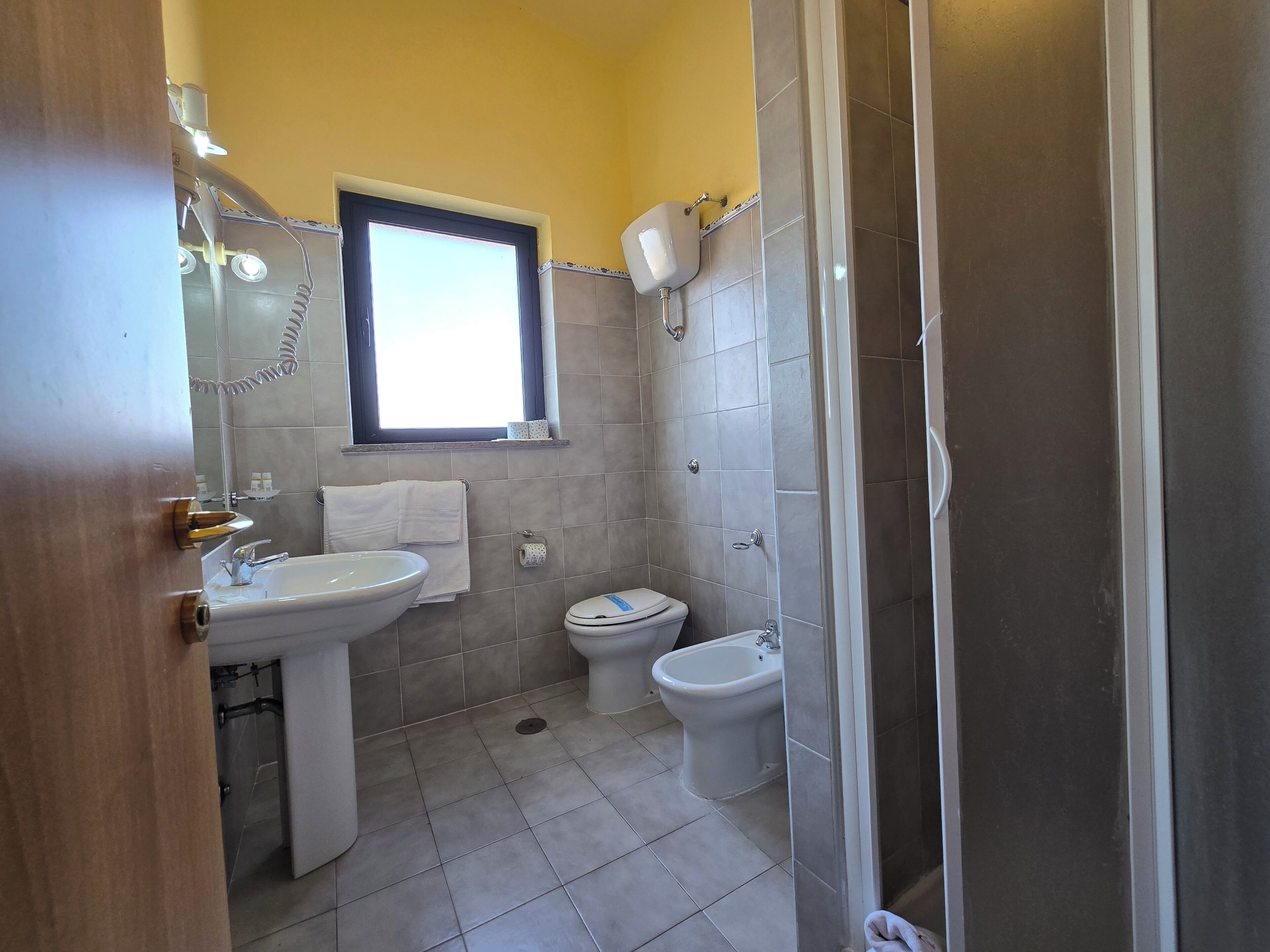 A bathroom with a sink, toilet, bidet, and a window.
