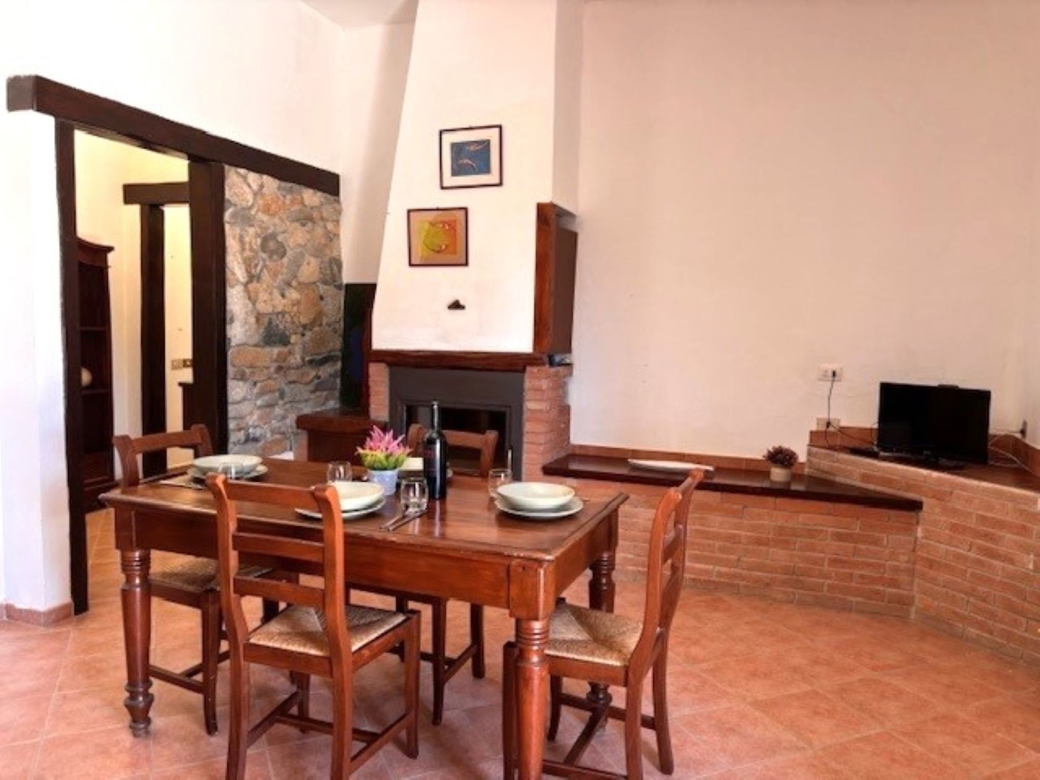 A dining area with a stone fireplace, a television, and a brick wall.