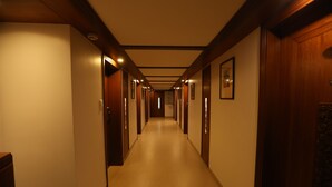 Un pasillo de hotel con puertas de madera, cuadros enmarcados en las paredes y suelo de baldosas.