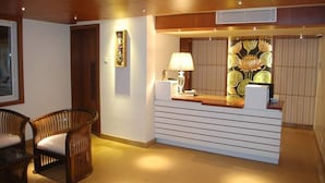 Un área de recepción con un mostrador de madera, una lámpara y una pared decorativa con motivos florales.