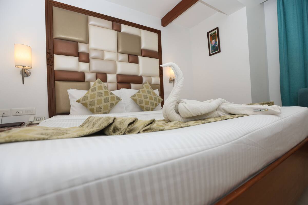 A neatly made bed with a swan-shaped towel, a headboard with a geometric pattern, and a bedside lamp.