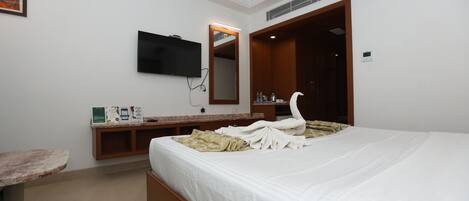 A hotel room with a bed, a television, a mirror, a vanity, and a small table.