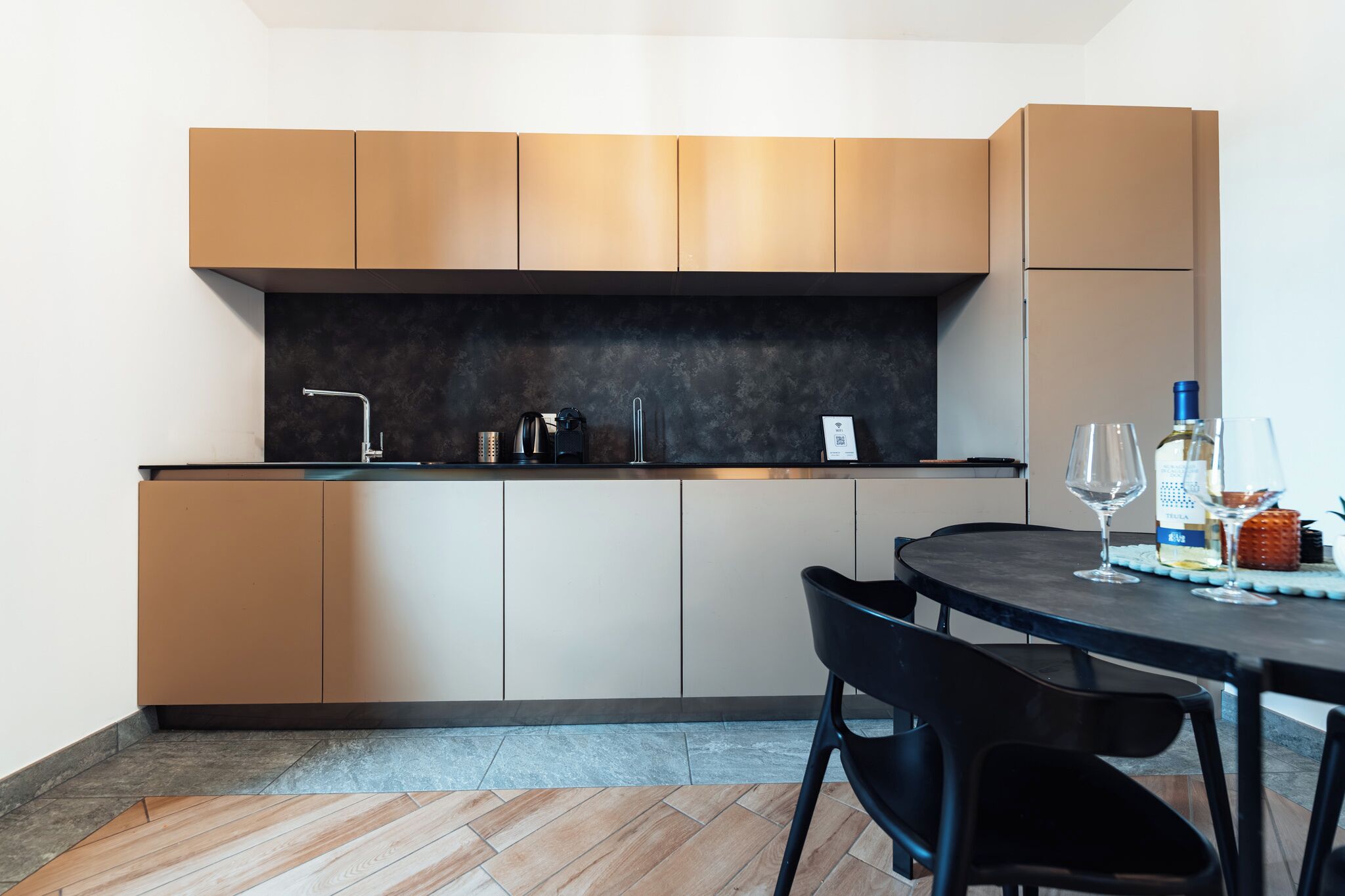 Eine moderne Küche mit dunkler Arbeitsplatte, beigen Schränken und einem Essbereich mit rundem Tisch und Stühlen.