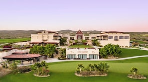Eine Golfakademie mit einem großen Gebäude, einer Terrasse und gepflegten Rasenflächen.