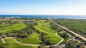 Ein Golfplatz mit Blick auf die Küste, ein großes Gebäude und eine Straße, die zum Meer führt.