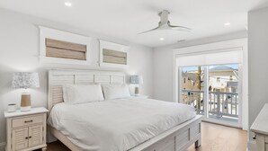 Un dormitorio con cama, mesitas de noche, ventilador de techo y vista a edificios a través de un ventanal.