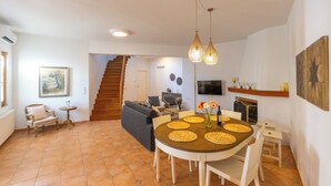 Een ruime woonkamer met een eettafel, stoelen, een bank en een trap naar een andere kamer.