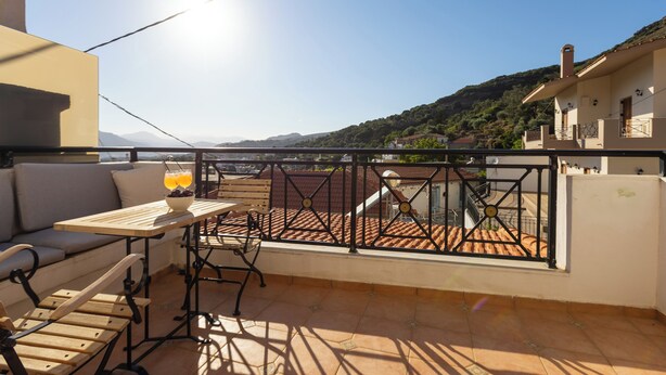 Een balkon met een tafel, stoelen, een bank en uitzicht op een heuvel.