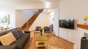 Een woonkamer met een bank, stoelen, een salontafel, een televisie en een trap.