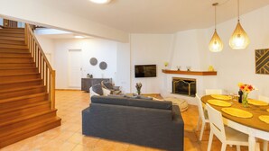 Een moderne woonkamer met een bank, eettafel en stoelen. Achtergrond is een trap zichtbaar.