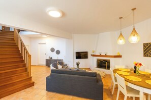 A modern living room with a sofa, dining table, and chairs. A staircase is visible in the background. - The Bridge House, 4BR Home for 10 with Terrace, Spili Rethymno (Spili)