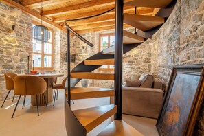 Ein modernes Interieur mit einer Wendeltreppe, Steinwänden und einem Essbereich mit Stühlen und einem Tisch.