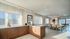Een moderne keuken met een groot eiland, een eethoek met stoelen en grote ramen.