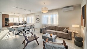 Een moderne woonkamer met een bank, salontafel en stoelen, een eethoek met tafel en stoelen, en een keuken op de achtergrond.