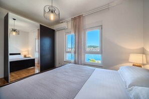 A modern bedroom with a large bed, a mirror, and a view of the sea. - Aurore's Place - Cozy Seaview Apartment (Okrug Gornji)
