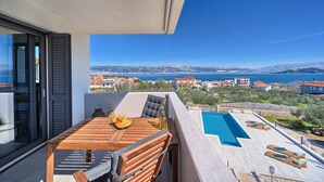 A balcony with a wooden table, chairs, and a view of a swimming pool and distant landscape. - One Bedroom Villa Ming (Slatine)