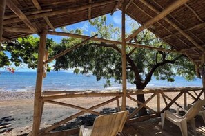 Une structure en bois située au bord de la plage, dotée d’un toit de chaume, qui offre de l’ombre et une vue sur la mer.