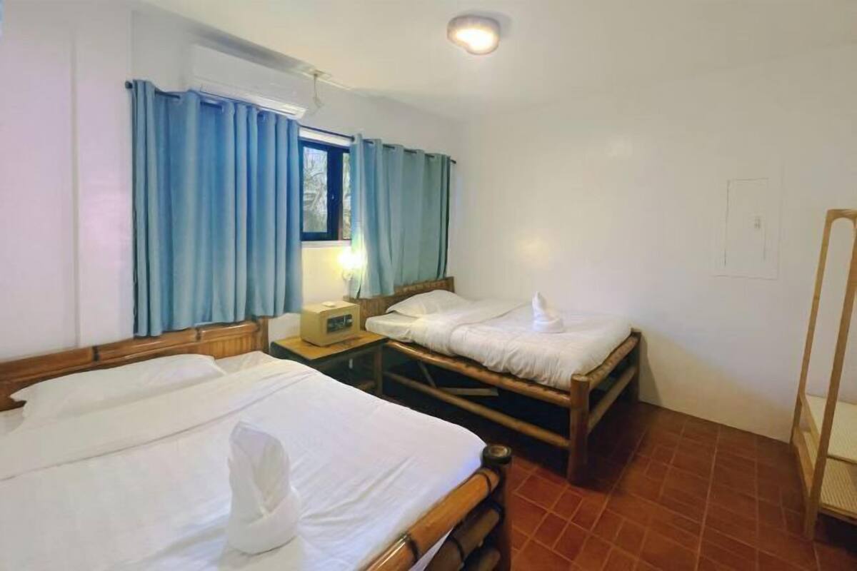 A room with two wooden beds, a nightstand with a lamp, and a window with blue curtains.