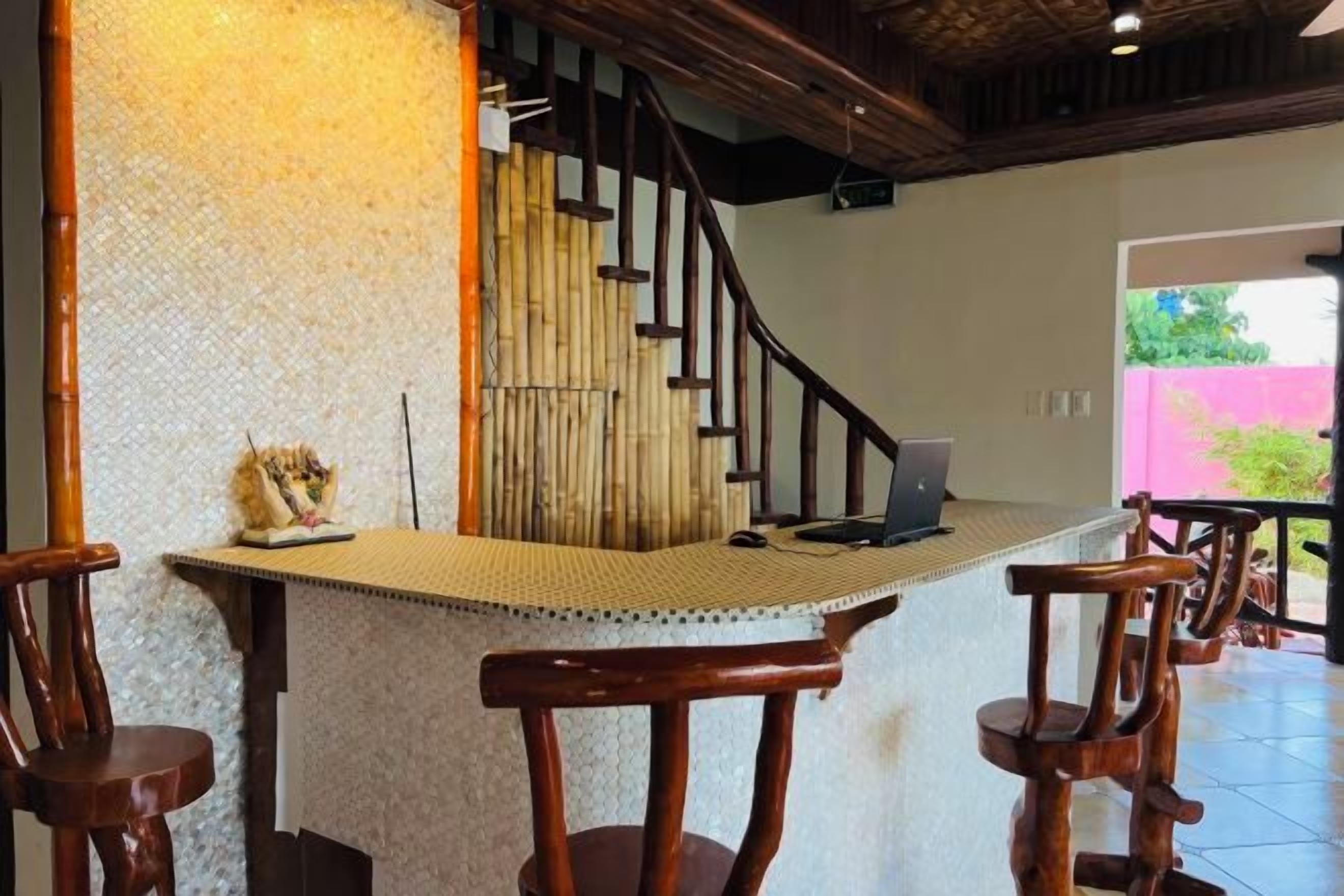 Una zona de bar con una laptop, sillas de madera y una escalera al fondo.