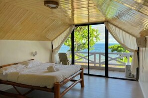 Una habitació amb llit, una cadira i vista al mar.