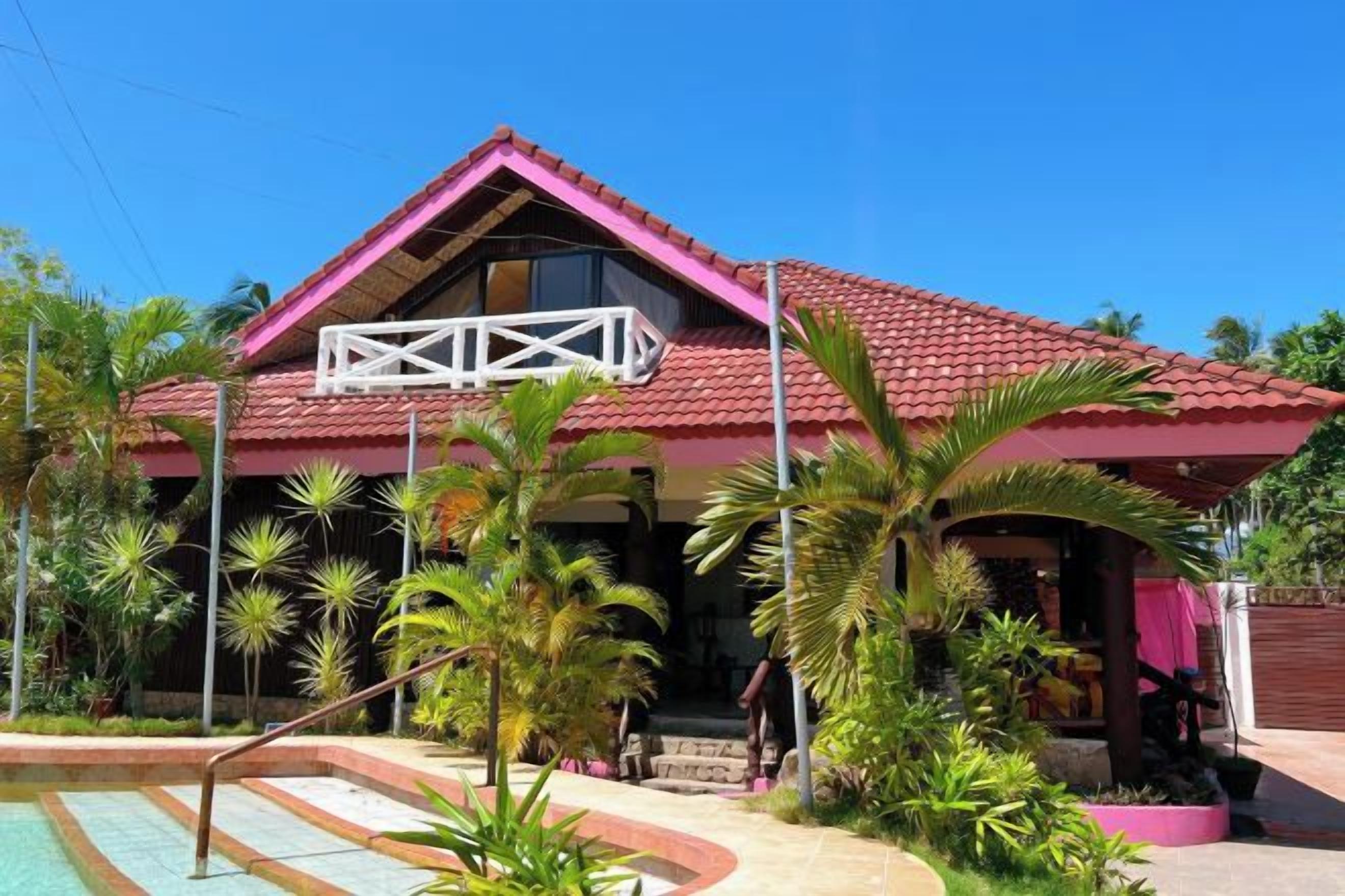 A two-story building with a red-tiled roof, a balcony, and a swimming pool.