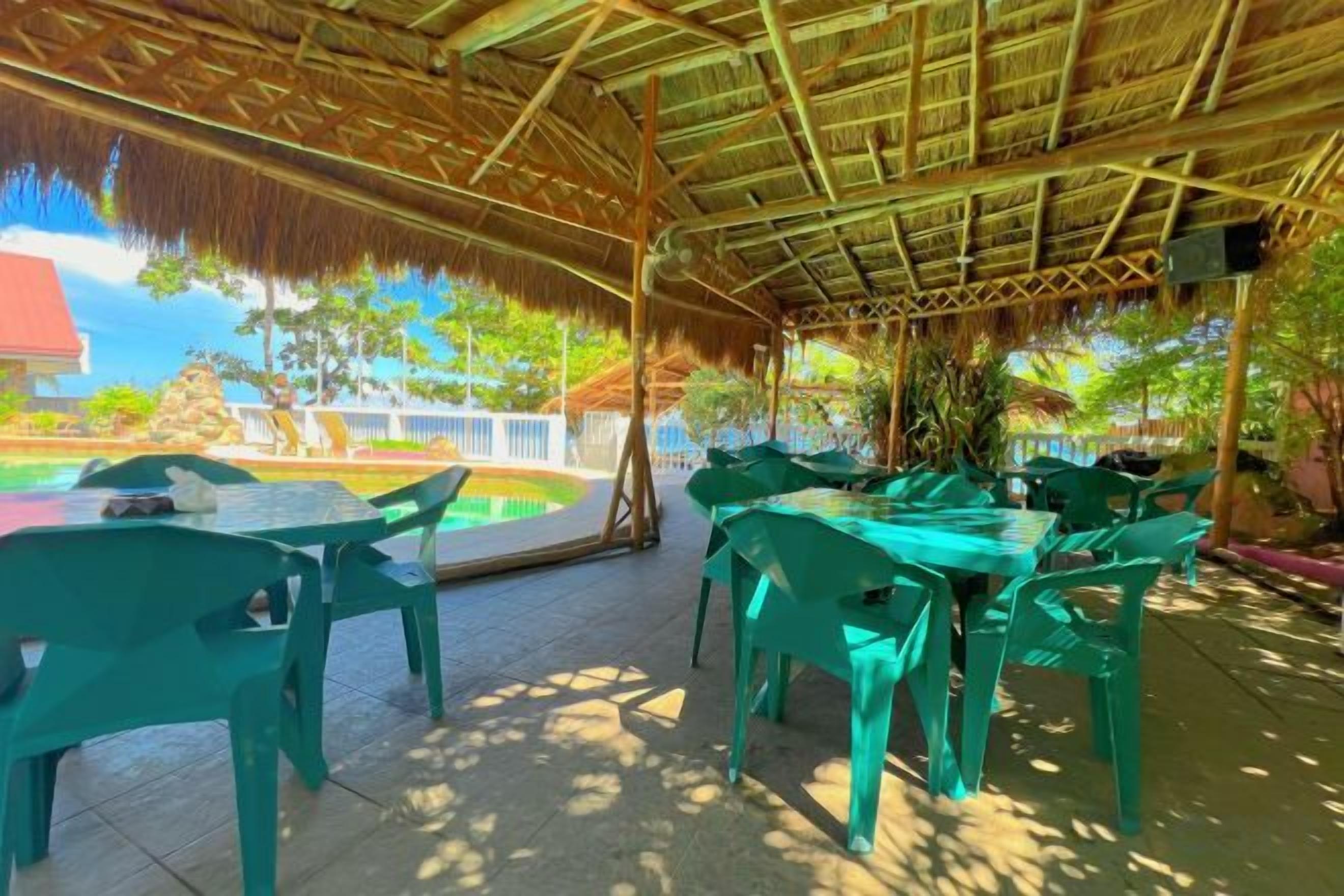 Un área de comedor al aire libre con mesas y sillas, una piscina y una estructura de techo de paja.