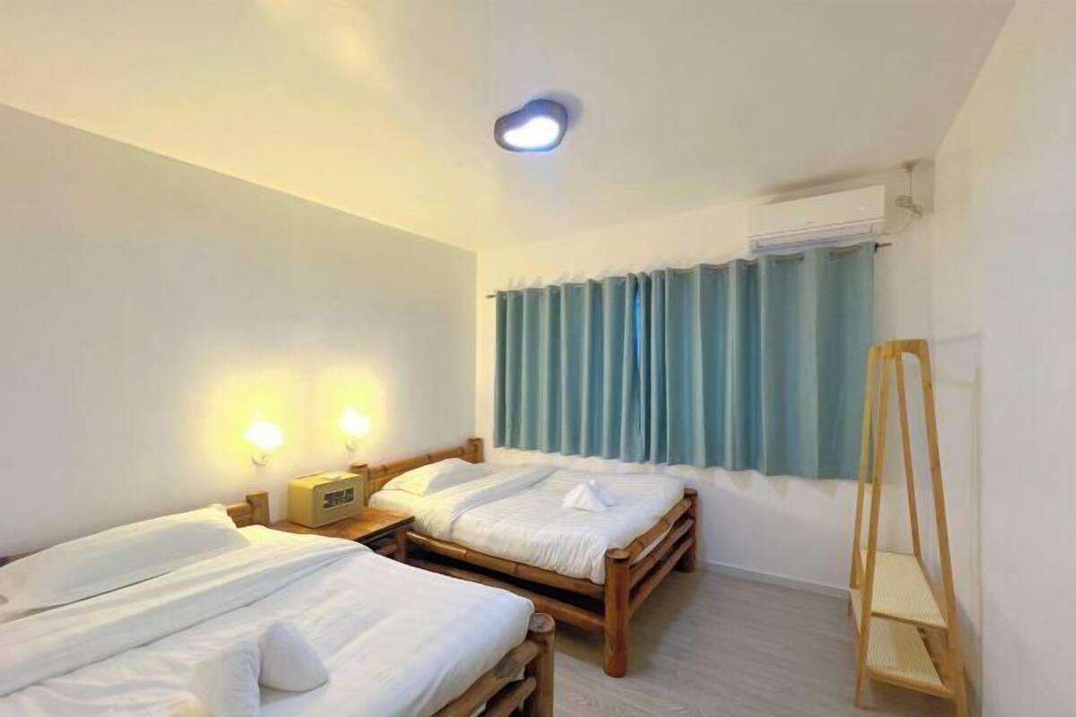A hotel room with two wooden beds, a standing lamp, an air conditioning unit, and a wooden ladder.