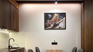 A kitchen with wooden cabinets, a white tiled backsplash, a black faucet, and a framed space-themed artwork on the wall. - Mountain Serenity — 5 min. to the ski lift (New Gudauri)