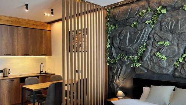 A modern room with a wooden desk, a bed with a headboard, and a wall with a rock-like texture and green plants. - Mountain Serenity — 5 min. to the ski lift (New Gudauri)