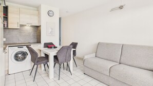 Ett kompakt bostadsutrymme med tvättmaskin, ett matbord med fyra stolar och en grå soffa.