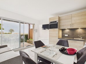 A modern kitchen with a built-in oven and microwave, a dining area with a table set for two, and a sliding glass door leading to a patio. - Sea view – Apartment for 4 with terrace (Sarzeau)