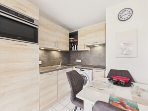 A compact kitchen with a built-in washer, a dining area with a table set for two, and a clock on the wall. - Sea view – Apartment for 4 with terrace (Sarzeau)