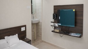 Una habitación de hotel con cama, espejo, lavamanos y televisor montado.