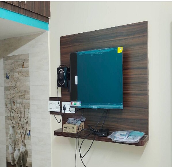 A wall-mounted TV on a wooden panel with a power strip and cables.